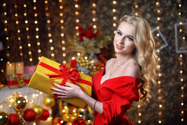 Una bionda intelligente con un vestito rosso tiene una scatola con un regalo per Natale. - Foto, immagini