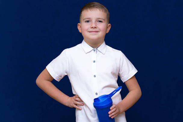 Portrait of happy little boy with water from plastic bottle on blue dark background - 写真・画像