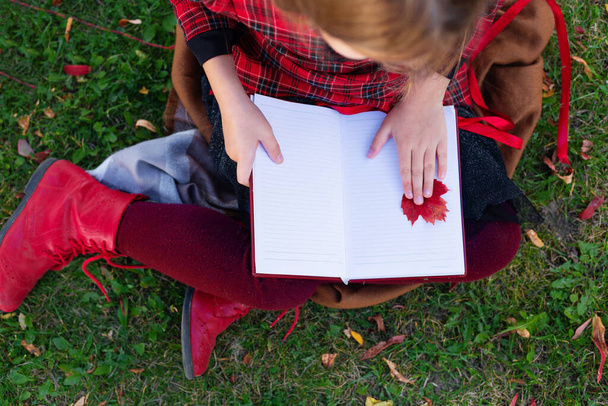 Dziewczyna siedzi na ziemi z notatnikiem w rękach.. - Zdjęcie, obraz
