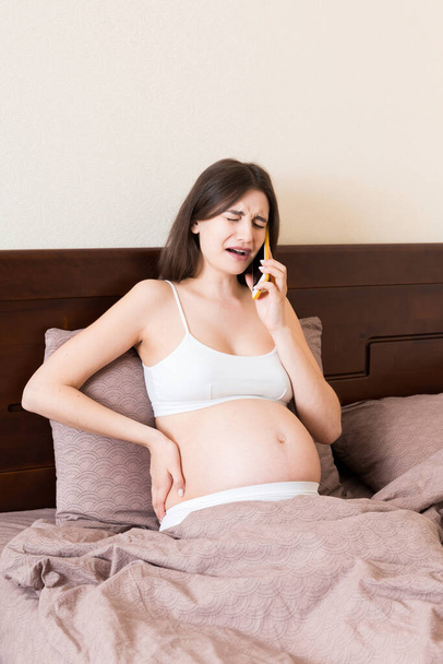 Duygusal hamile kadın evde yatakta cep telefonuyla ağlıyor ve konuşuyor.. - Fotoğraf, Görsel
