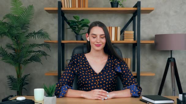 Χαμογελώντας θετική όμορφη γυναίκα δάσκαλος δάσκαλος κάθεται στην καρέκλα στο τραπέζι στο γραφείο στο σπίτι φοράει ασύρματα ακουστικά φαίνεται κάμερα ακούγοντας φοιτητής στο συνέδριο συνομιλίας κλήση βίντεο, web cam οθόνη έννοια - Πλάνα, βίντεο