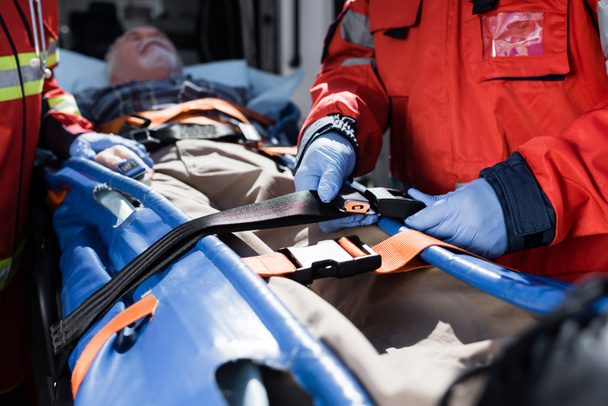 Selective focus of paramedic locking belt near patient on stretcher near ambulance car - Φωτογραφία, εικόνα