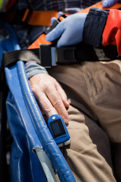 Vue recadrée de l'ambulancier dans des gants en latex verrouillage ceinture de civière près du patient avec moniteur de fréquence cardiaque - Photo, image