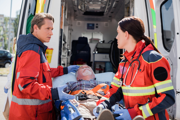 Szelektív fókusz a mentős mutató beteg hordágyon közeli kolléga latex kesztyű és mentő autó  - Fotó, kép