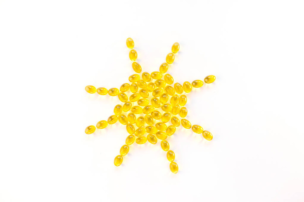 Kreatives Konzept Vitamin D3, Sonnenschein Vitamin. Kapseln sind in Form der Sonne auf weißem Hintergrund ausgelegt. Kopierraum, Minimalismus, Draufsicht. - Foto, Bild