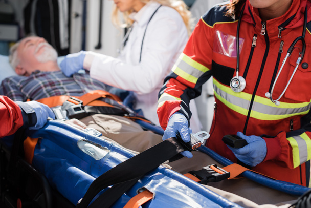 Focus selettivo delle cinghie paramediche di contenimento della barella vicino al paziente e ai colleghi all'aperto  - Foto, immagini