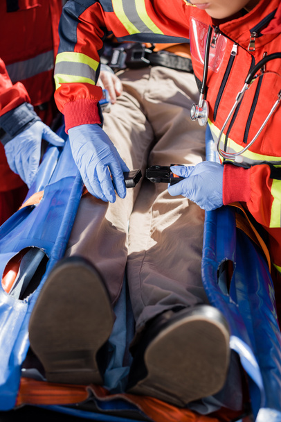 Selective focus of paramedic locking belts of stretcher near patient and colleague in latex gloves   - Foto, immagini