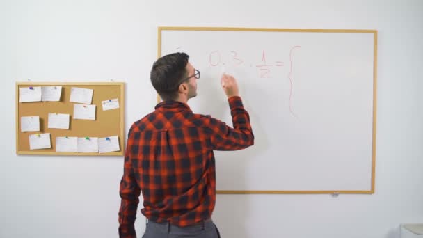 Giovane insegnante di matematica maschile che scrive equazioni matematiche sulla lavagna bianca usando il pennarello rosso per la classe online, tutor di e-learning - Filmati, video