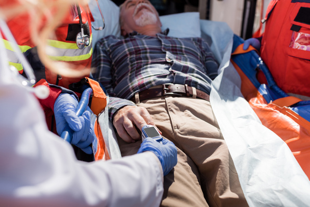 Selektiver Fokus des Arzt-Nüchternen-Pulsmessgeräts auf Patienten in der Nähe von Sanitätern und Rettungswagen  - Foto, Bild