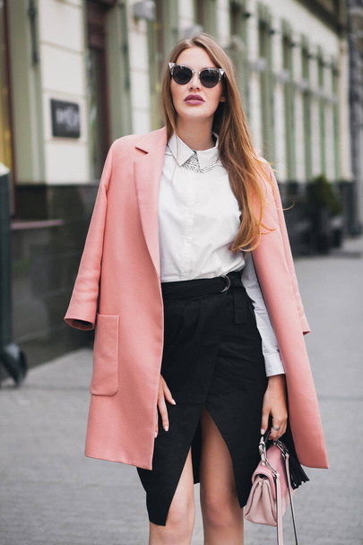 cool young stylish beautiful woman walking in street, wearing pink coat, purse, sunglasses, white shirt, black skirt, fashion outfit, autumn trend, smiling happy, accessories - Fotoğraf, Görsel