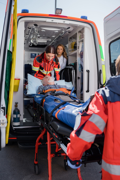 Selective focus of paramedics holding stretcher with senior patient near ambulance car  - Photo, Image
