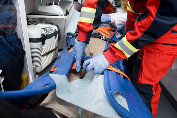 Vista recortada de los cinturones de sujeción paramédicos de la camilla cerca del paciente en el coche de ambulancia  - Foto, Imagen