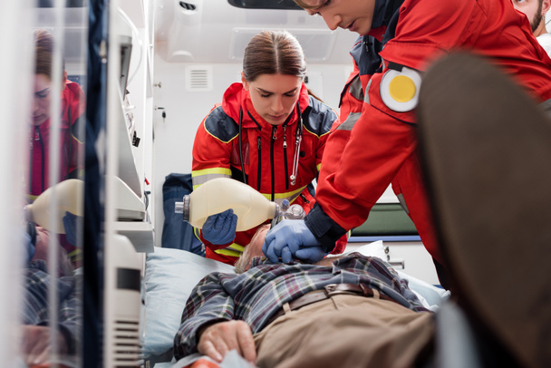 Selective focus of paramedics in uniform doing cardiopulmonary resuscitation to man during first aid  - Foto, imagen