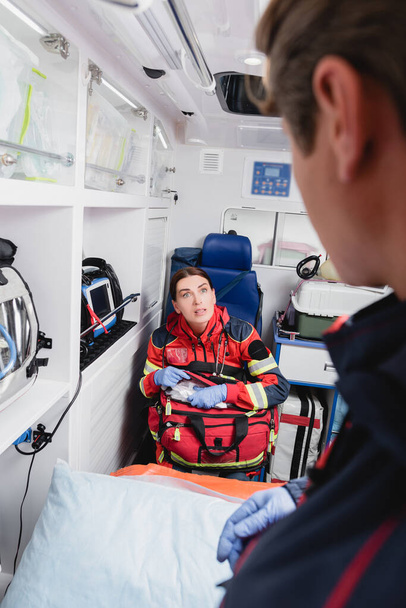 Focus selettivo del paramedico con kit di pronto soccorso guardando il collega in ambulanza  - Foto, immagini
