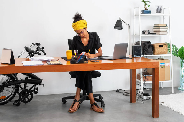 Kuvattu nuori latino nainen työskentelee kotona toimistossa kannettavan tietokoneen ja asiakirjojen kanssa - Valokuva, kuva