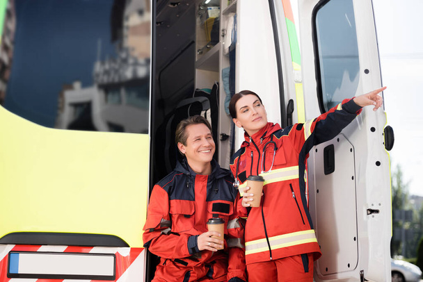 Paramedico punta con dito vicino collega con caffè per andare e auto ambulanza  - Foto, immagini