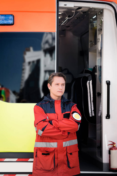 Paramedic with crossed arms standing near ambulance auto outdoors  - Фото, зображення