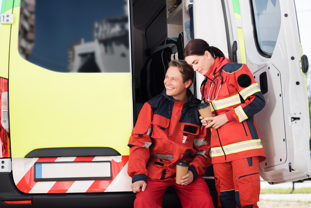 Sanitäter in Uniform halten Kaffee in der Nähe von Rettungswagen  - Foto, Bild