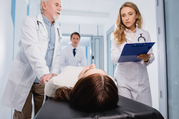 Valikoiva painopiste lääkärit leikepöydällä kävely lähellä potilaan paarit klinikalla  - Valokuva, kuva