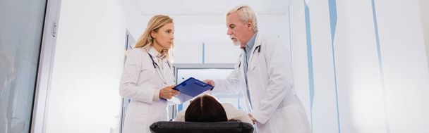 Nagłówek strony internetowej lekarzy ze stetoskopami i schowkiem stojącym w pobliżu chorej kobiety na noszach w klinice  - Zdjęcie, obraz