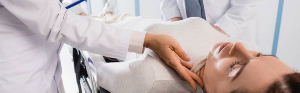 Panoramaaufnahme eines Arztes, der den Puls der Frau auf einer Trage in der Klinik überprüft  - Foto, Bild