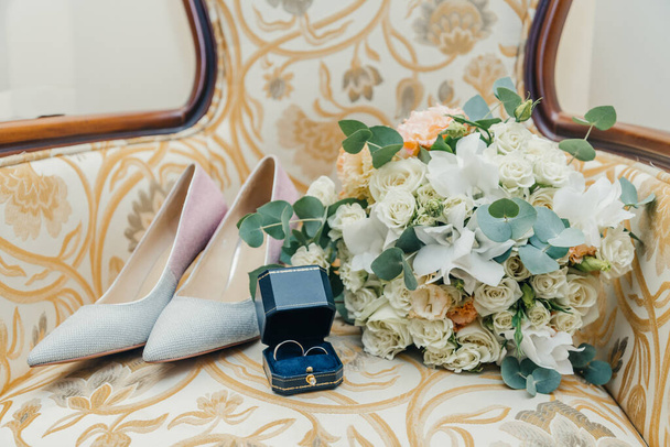 fehér arany jegygyűrűk egy dobozban és egy menyasszonyi csokor finom rózsa és zöld - Fotó, kép