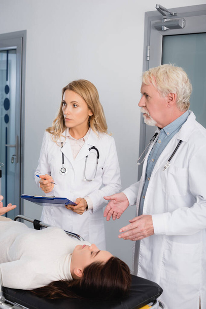 Вибірковий фокус лікарів з буфері, які дивляться на колегу поблизу пацієнта в клініці
  - Фото, зображення