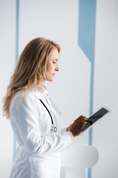 Боковой вид врача-блондинки с помощью цифрового планшета в клинике  - Фото, изображение