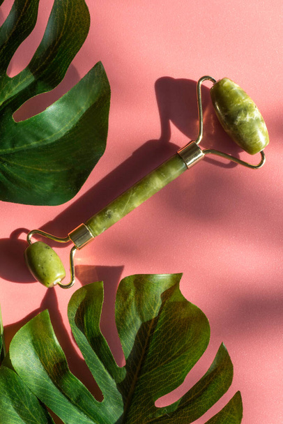 Rolo de jade com folhas monstera na superfície ensolarada com sombras, conceito de beleza holística verde, anti-envelhecimento, anti-rugas ferramentas de cuidados da pele beleza de pedra natural - Foto, Imagem