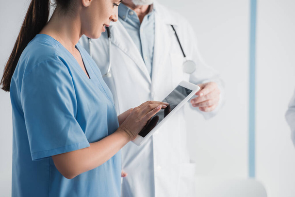 Vista ritagliata dell'infermiere utilizzando tablet digitale vicino al medico in clinica  - Foto, immagini