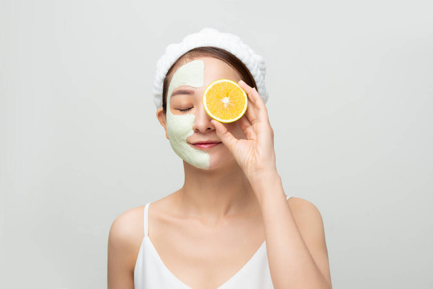 Pretty Asian young woman mask moisturizing and rejuvenating clean skin peeling while holding orange pieces over white background. - Foto, immagini