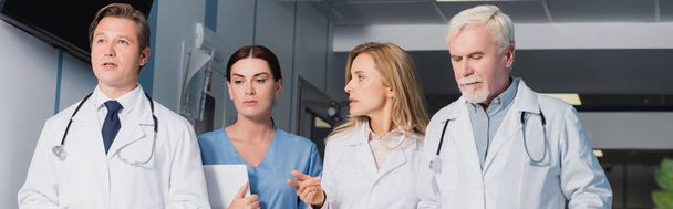Az orvos horizontális terménye ujjal mutogat a kollégák és a nővér közelében, digitális tablettával  - Fotó, kép
