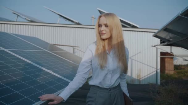 Gün batımında iki güneş paneli arasında yürüyen bir kız. Kadın yatırımcı resmi beyaz gömlek giyer. Ev için bedava elektrik. Gezegenin sürdürülebilirliği. Yeşil enerji. - Video, Çekim