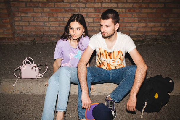 young stylish hipster couple in love, swag outfit, jeans, embrace, cool accessories, sitting on ground against brick wall, happy, having fun - Фото, зображення