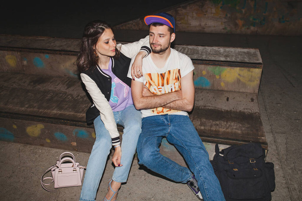 young stylish hipster couple in love, swag outfit, jeans, embrace, cool accessories, sitting happy, having fun - Photo, image