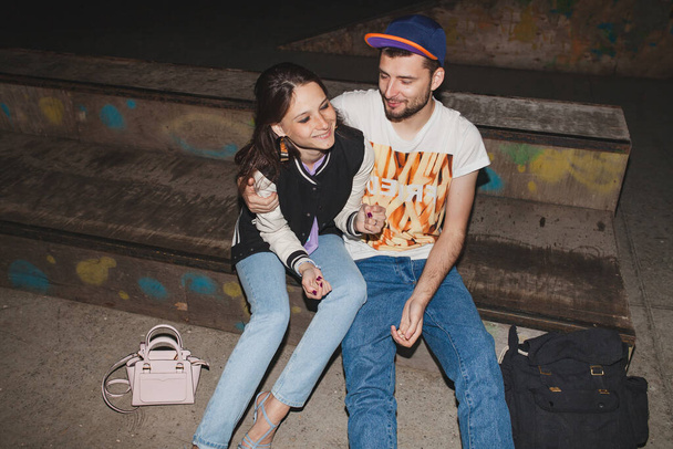 young stylish hipster couple in love, swag outfit, jeans, embrace, cool accessories, sitting happy, having fun - Foto, afbeelding