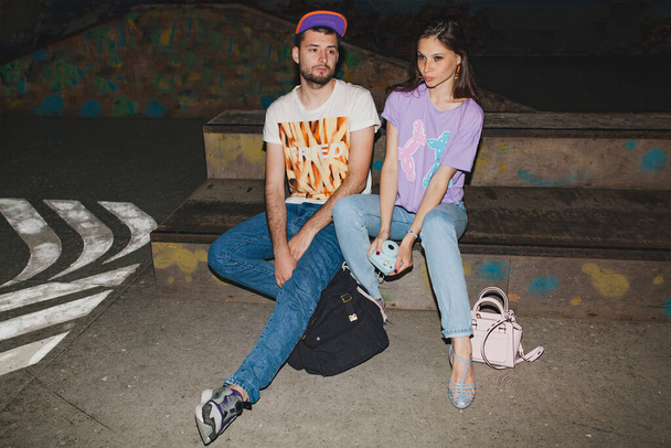 cool young stylish hipster couple in love, swag outfit, jeans, embrace, cool accessories, sitting happy, having fun - Photo, image