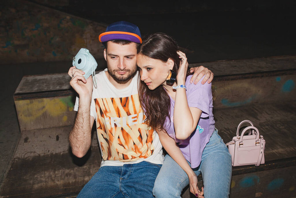young stylish hipster couple in love, swag outfit, jeans, embrace, cool accessories, sitting happy, having fun, photo camera - Foto, Bild