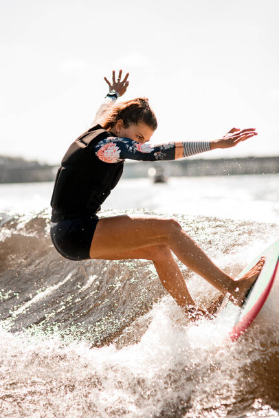 athletic woman stand on surf style wakeboard and ride up on splashed river wave. - Фото, зображення