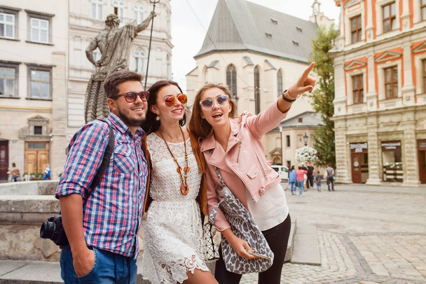 young hipster company of friends traveling, vintage style, europe vacation, sunglasses, old city center, happy positive mood, smiling, embracing, pointing finger, looking forward - Фото, изображение
