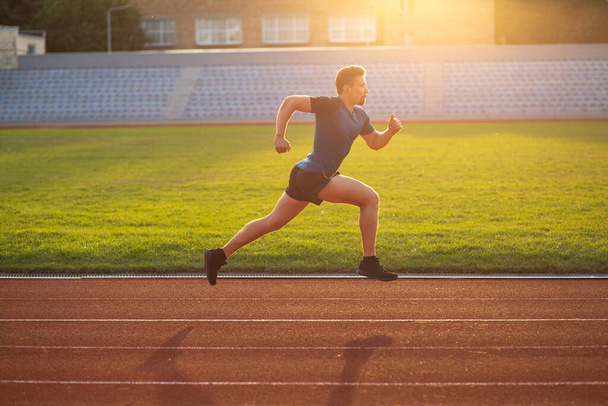 Young athlete man wears sport apparel running at the stadium with sun glare. Space for text - Photo, Image