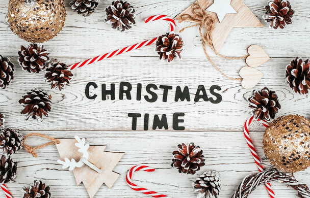 Christmas lettering made of black wooden letters surrounded by pine cones and toys on a white wooden background. - 写真・画像