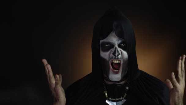 Sinister man with skeleton makeup in hood making angry faces, looking at camera, trying to scare - Footage, Video