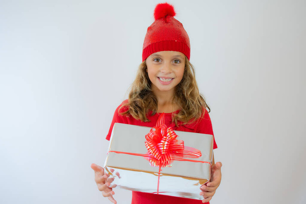 Picture of happy little girl child standing isolated over white background. Looking camera holding gift box surprise. - Photo, Image