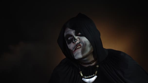 Gruseliger, verrückter Mann mit Skelett-Make-up in Kapuze macht wütende Gesichter, schüttelt den Kopf, versucht Angst zu bekommen - Filmmaterial, Video