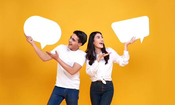 Smiling happy Asian couple holding blank speech bubbles on yellow background. - Photo, Image