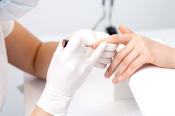 Manikúra mistr v ochranných rukavicích nanášení béžové lak na nehty samice v salonu krásy - Fotografie, Obrázek