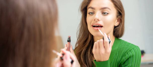 Beautiful young caucasian woman applying gloss to the lips looking in the mirror - Foto, Imagen