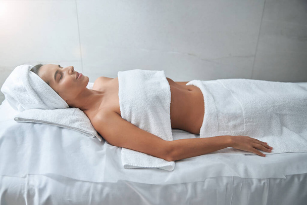 Beautiful young woman lying on massage table in spa salon - Photo, Image