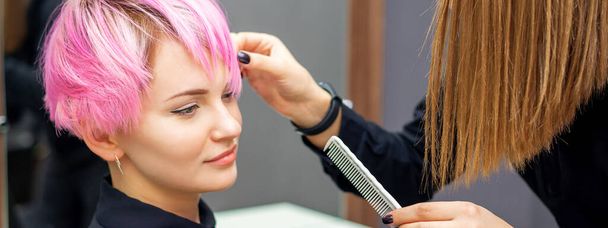 Young woman receiving short pink hairstyle by female hairdresser in beauty salon - Photo, Image